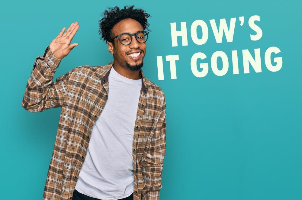 تصویر پسری رنگین گوست با موهای فر و عینک که لبخند زده و یک دستش را بالا آورده است