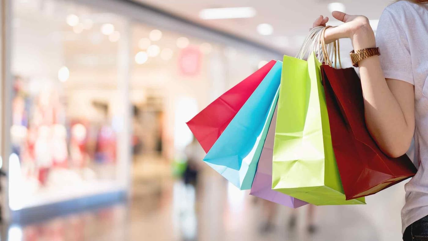 چندین کیسه خرید رنگارنگ در دستی که داخل یک پاساژ است