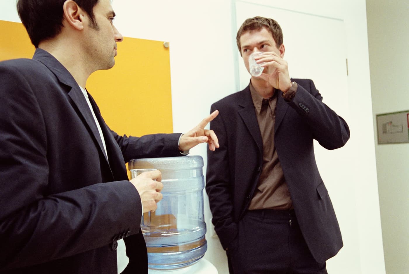 دو همکار مرد که کنار دستگاه آبریز ایستاده و آب مینوشند.