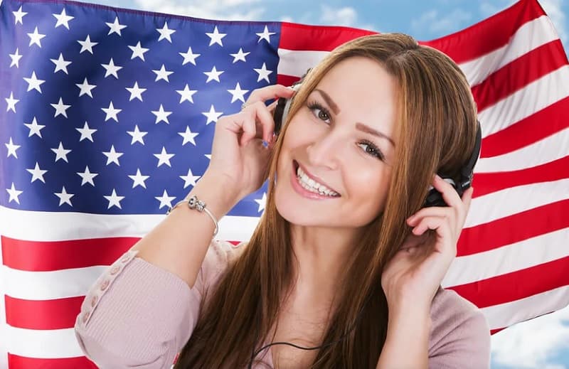 دختر جوانی با هدست مقابل پرچم آمریکا آهنگ گوش می‌کند