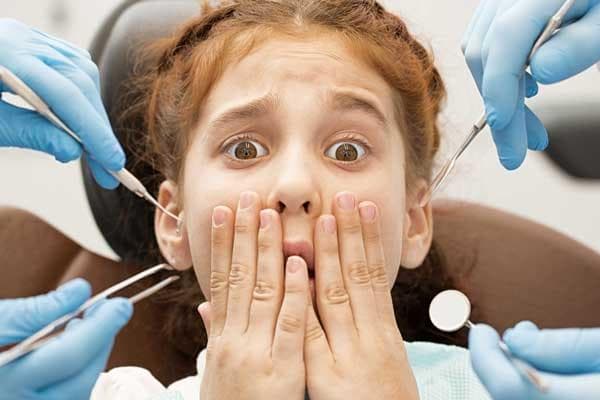 دختری ترسیده در مطب دندان‌پزشکی که با دست‌هایش دهانش را پوشانده
