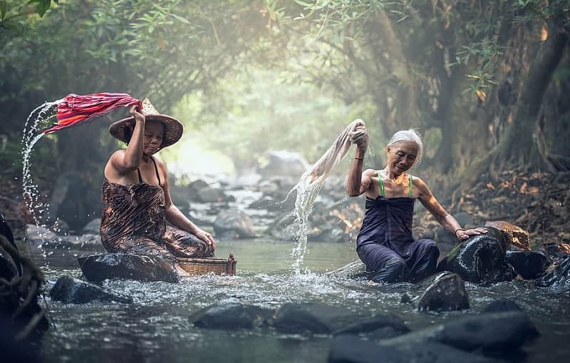 تصویر دو زن که در داخل رودخانه لباس می‌شوییند.