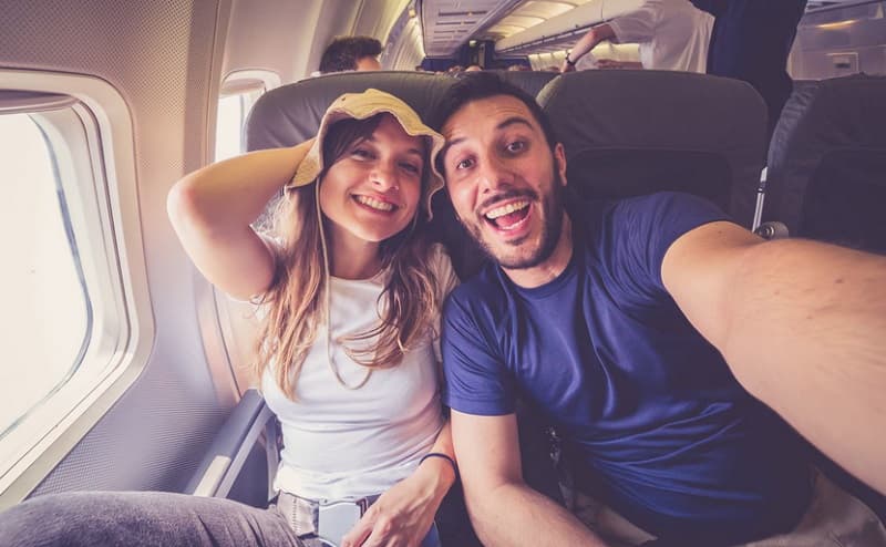 زن و مرد جوانی روی صندلی هواپیما از خود سلفی می‌گیرند.