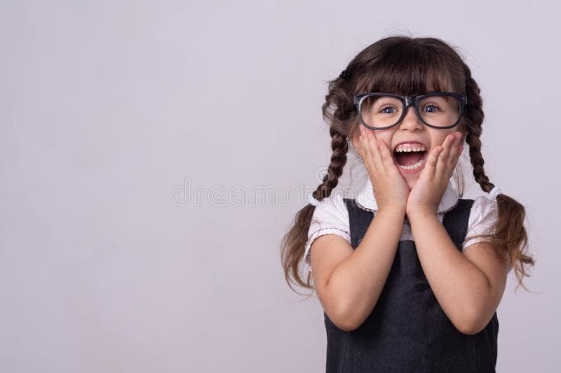 دختربچه‌ای عینکی با موهای خرگوشی که خوشحال است و گونه‌های خود را با دستانش گرفته