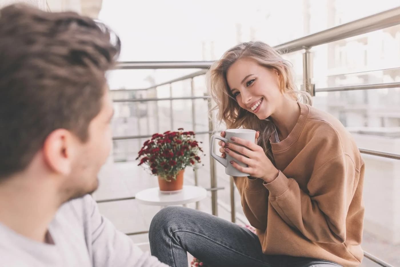 زن و مرد جوانی روی ایوان نشسته و با لبخند به هم نگاه می‌کنند و قهوه می‌نوشند