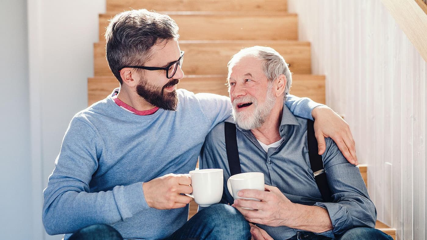 مرد جوان و پیرمردی روی راه‌پله چوبی نشسته و فنجان‌های سفیدی به دست دارند و به یک‌دیگر با لبخند نگاه می‌کنند.